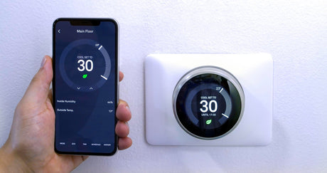 Close-up of person using mobile phone smart thermostat on wall