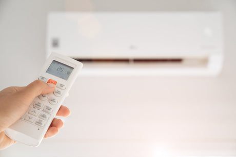 Woman hand holding remote controller directed on the air conditioner inside the room