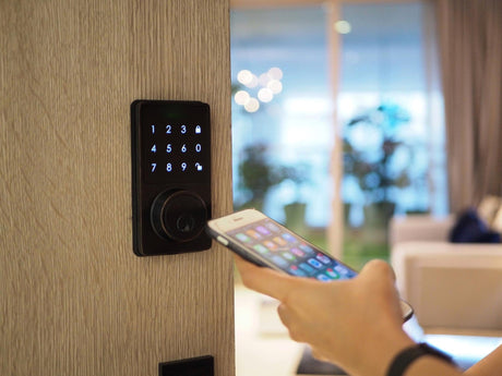 Cropped hand unlocking door with mobile phone at home